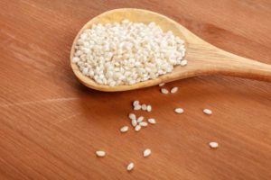 Close-up of a wooden spoon filled with authentic Spanish Calasparra rice for paella cooking, placed on a wooden surface.