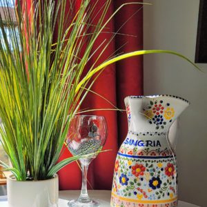 Colorful indoor scene with a vibrant green plant, an empty wine glass, and a decorative sangria pitcher against red curtains.
